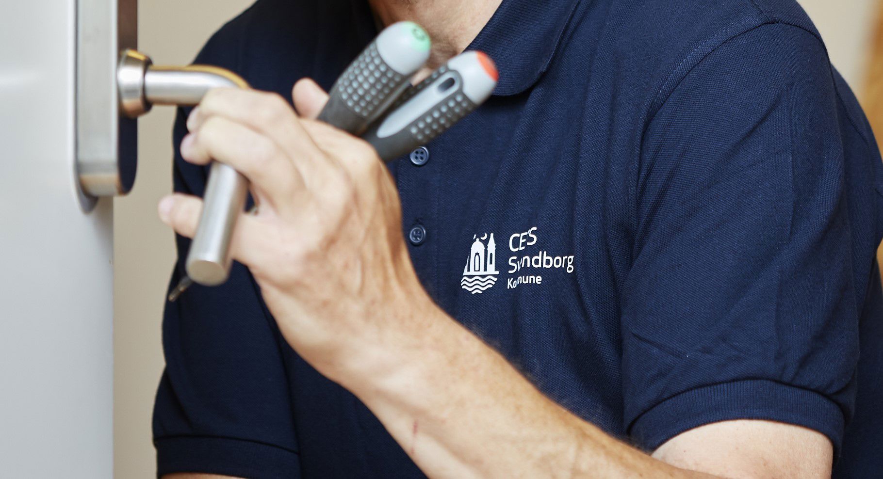 Hænder med værktøj som holder om et dørhåndtag.