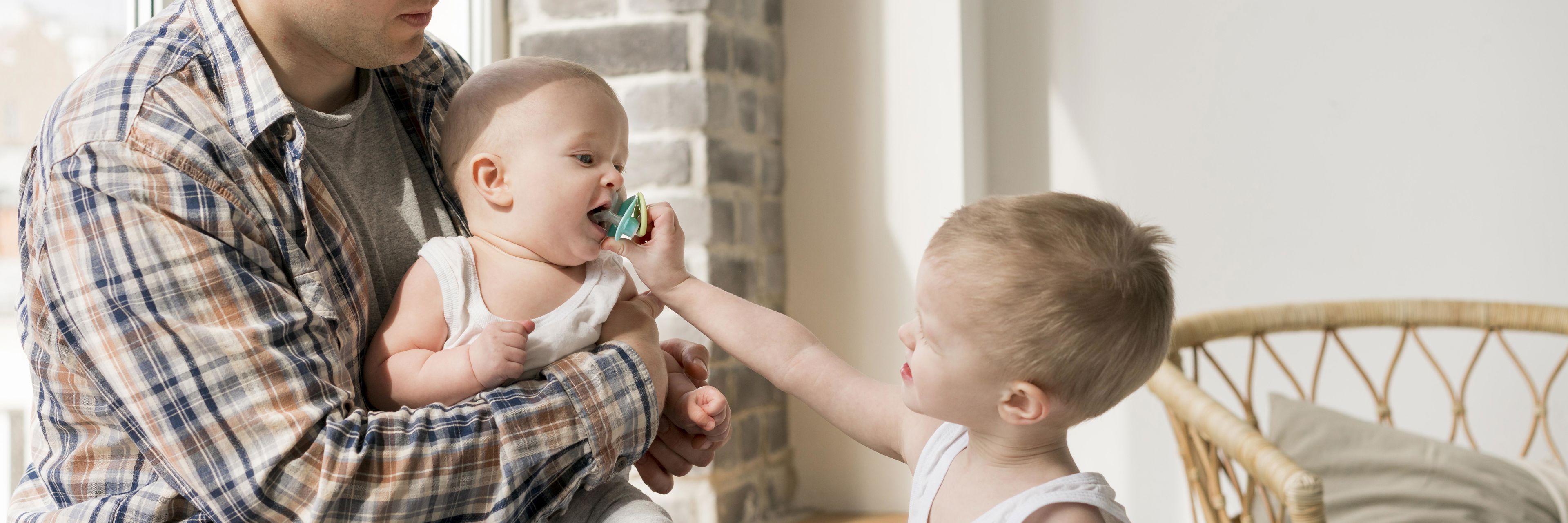 Stående dreng giver baby, der sidder hos far, sut i munden