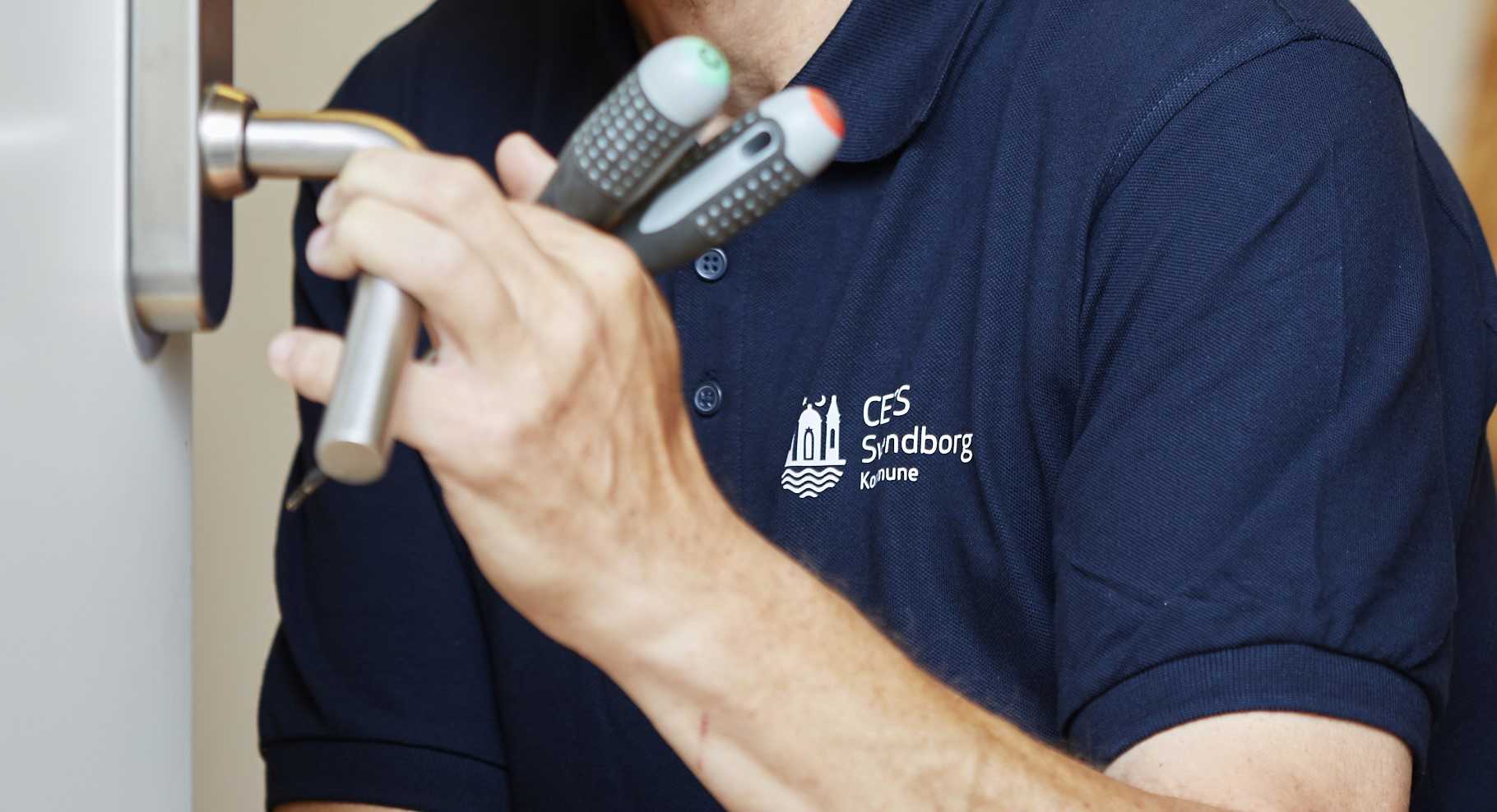 Hænder med værktøj som holder om et dørhåndtag.