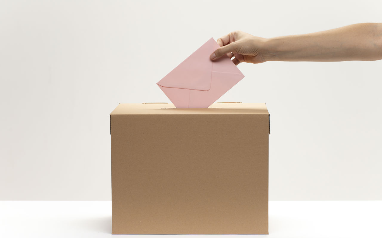 En kvindelig hånd putter en konvolut i en stemmekasse