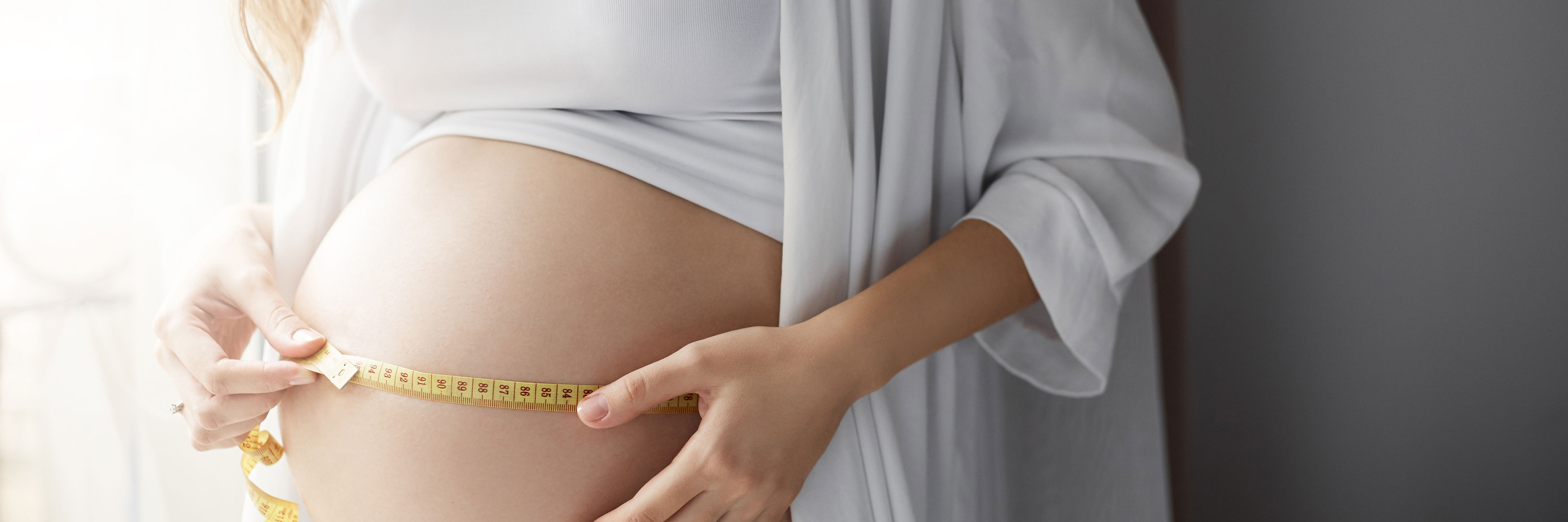 Gravid kvinde måler sin mave med en cemtimetermål