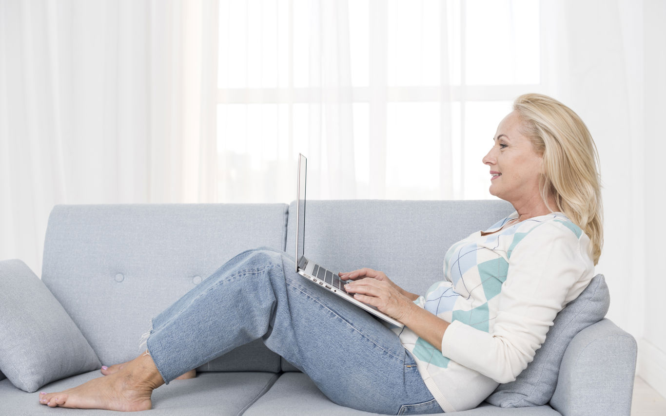 Dame, der sidder på sofa med opslået pc på lårene