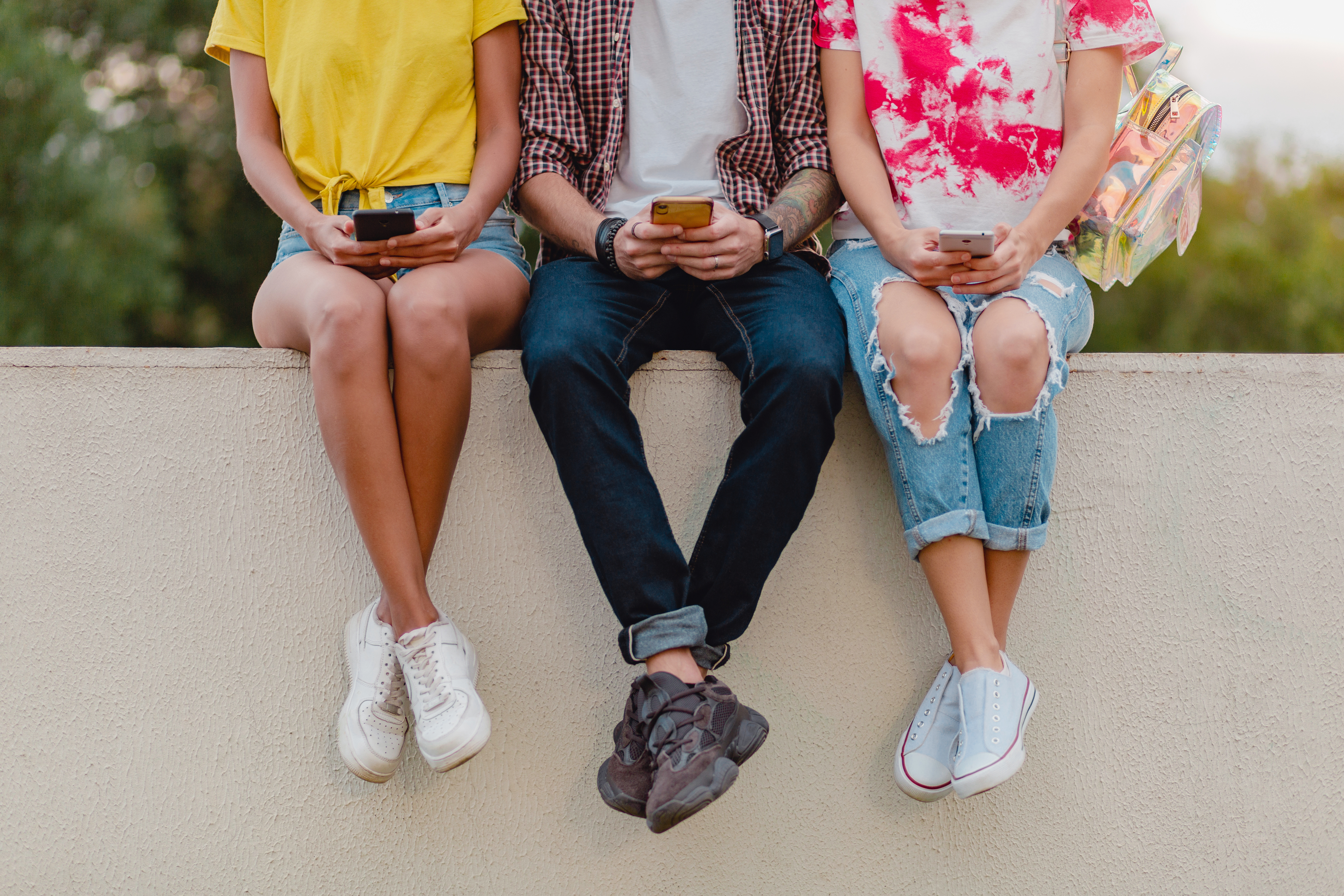 Tre mennesker sidder på en mur med deres smartphones i hånden
