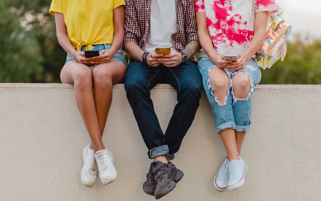 Tre mennesker sidder på en mur med deres smartphones i hånden