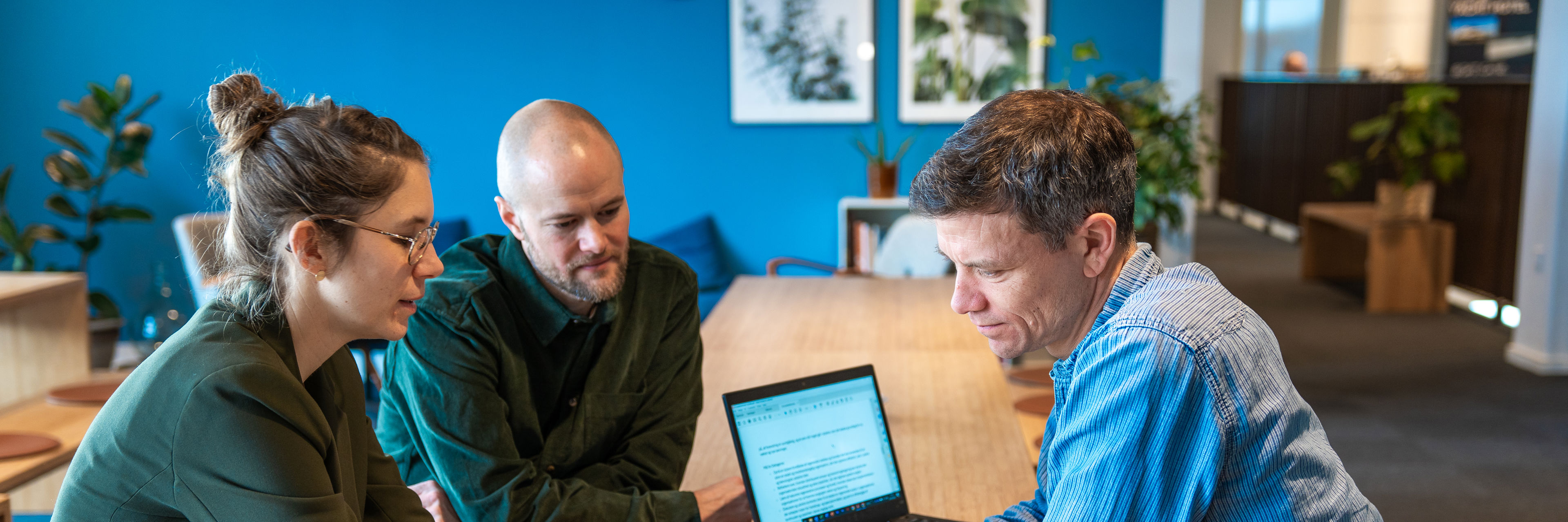 Tre personer der sidder ved et bord med en computer