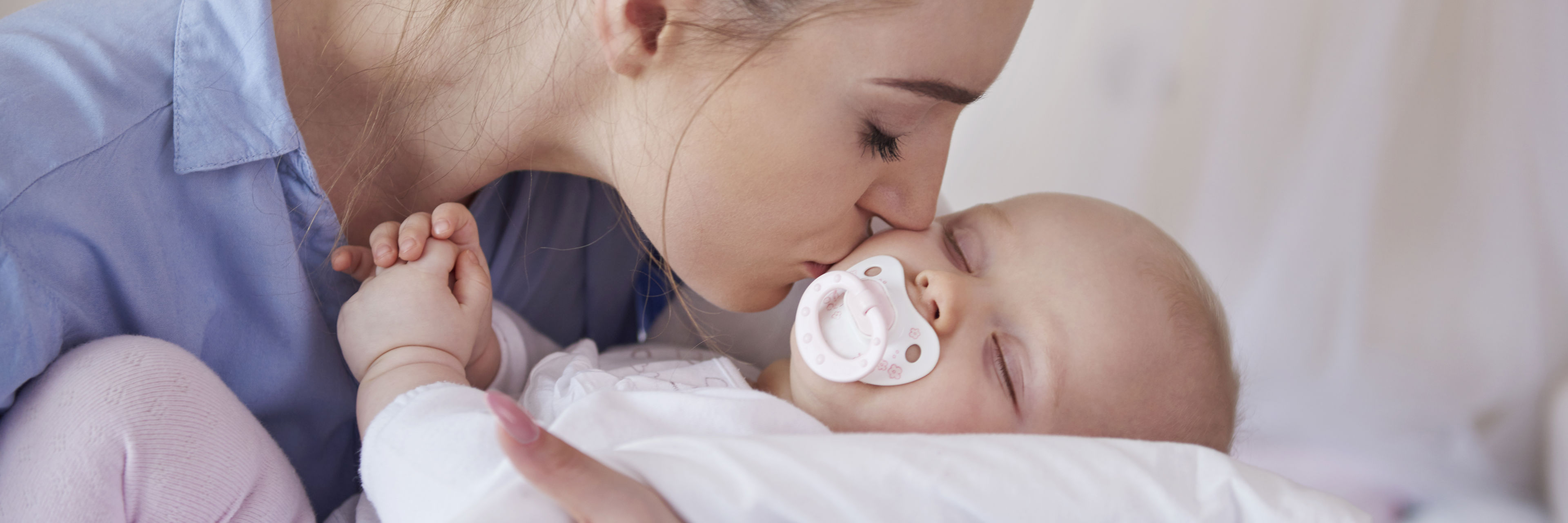 Kvinde kysser baby, med sut i munden, på kinden