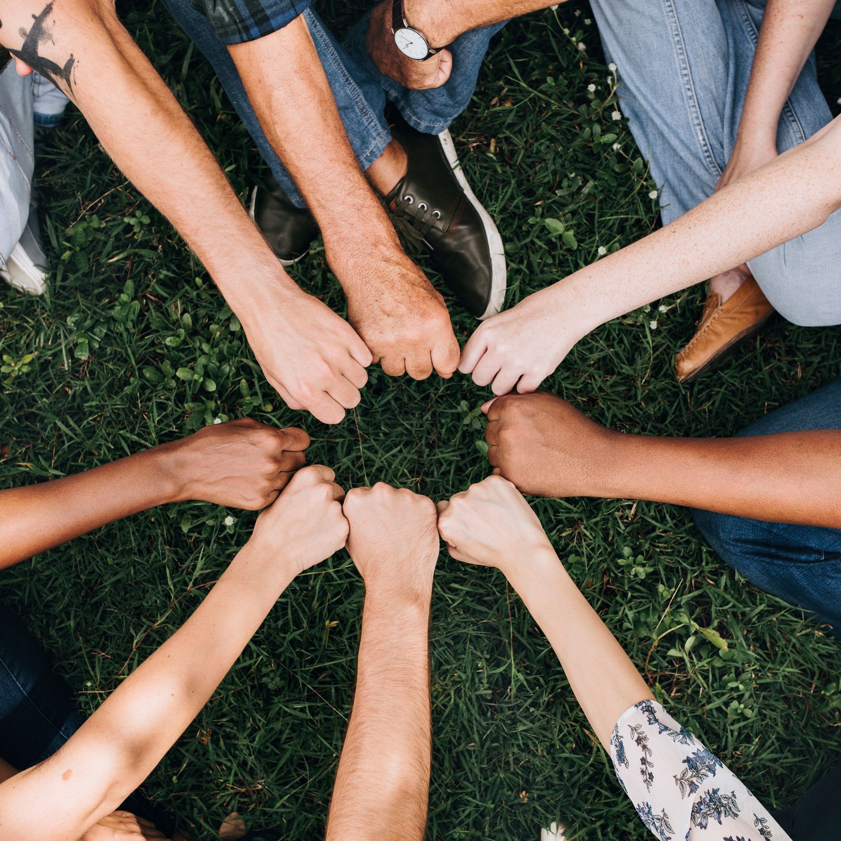 Forskellige mennesker rækker deres knyttede hænder ind mod hinanden, så de danner en cirkel. Billedet signalerer fællesskab og sammenhold.