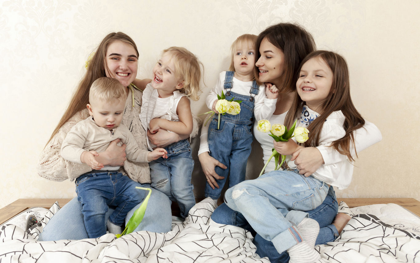 To kvinder og 4 børn sidder sammen i en seng