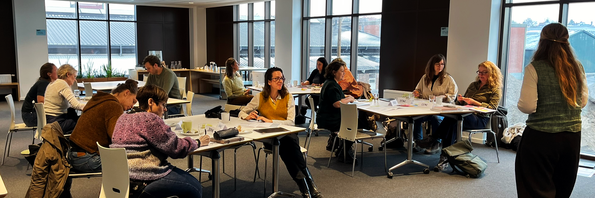 Kvinder og mænd ved borde i et mødelokale