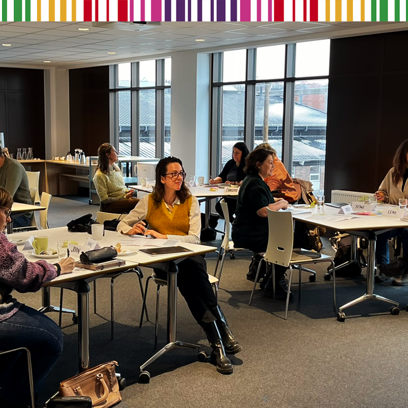 Kvinder og mænd ved borde i et mødelokale