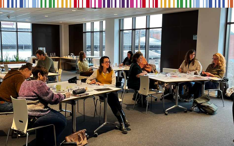 Kvinder og mænd ved borde i et mødelokale