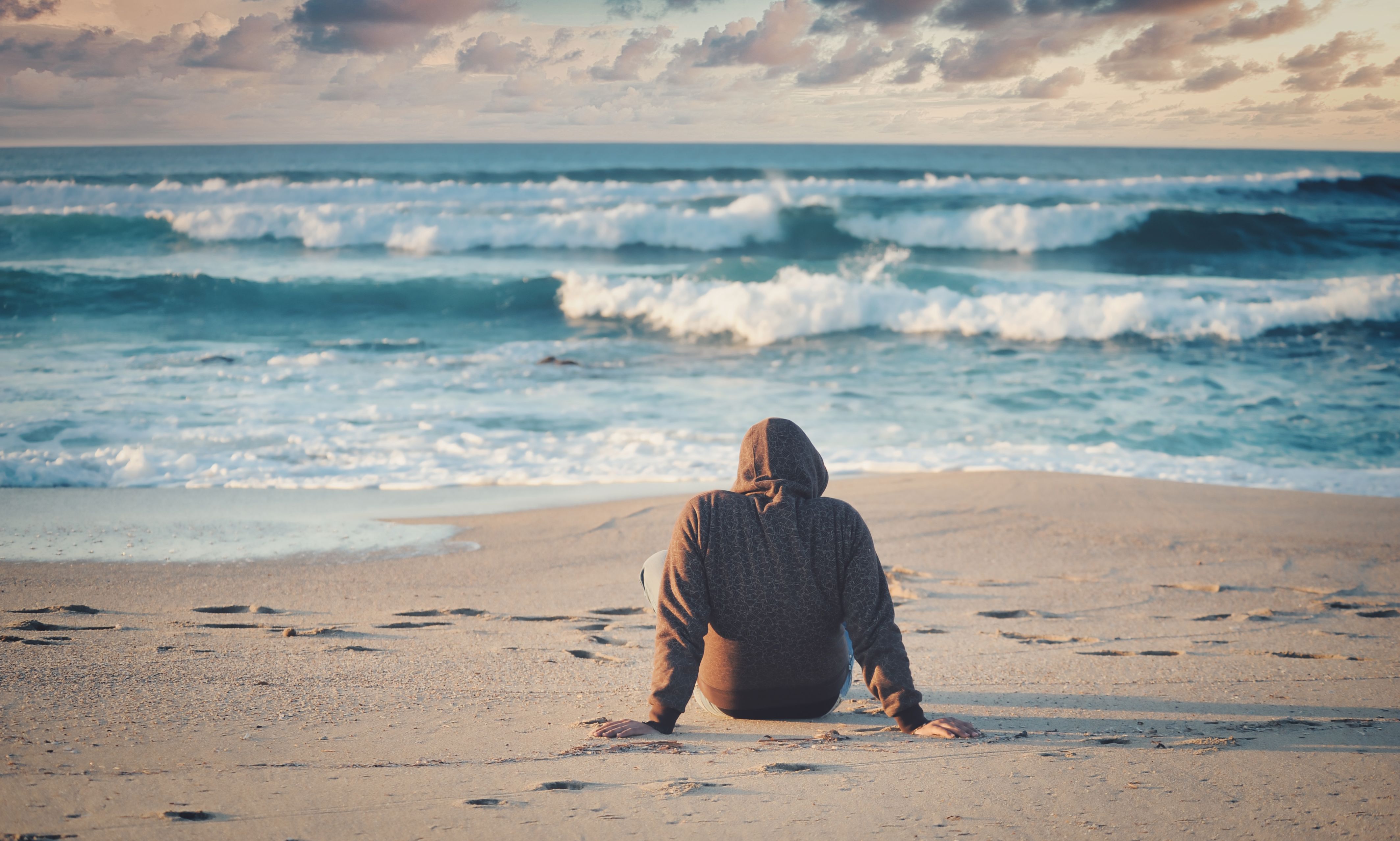 Person, der sidder med ryggen til og kigger på havets bølger