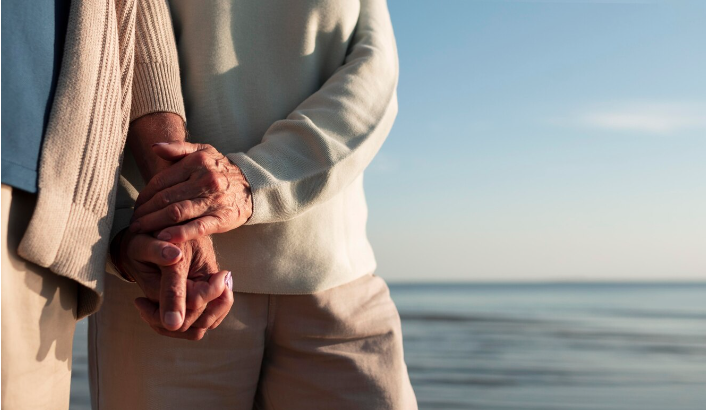 Ældre par hænder i hånden med havet i baggrunden
