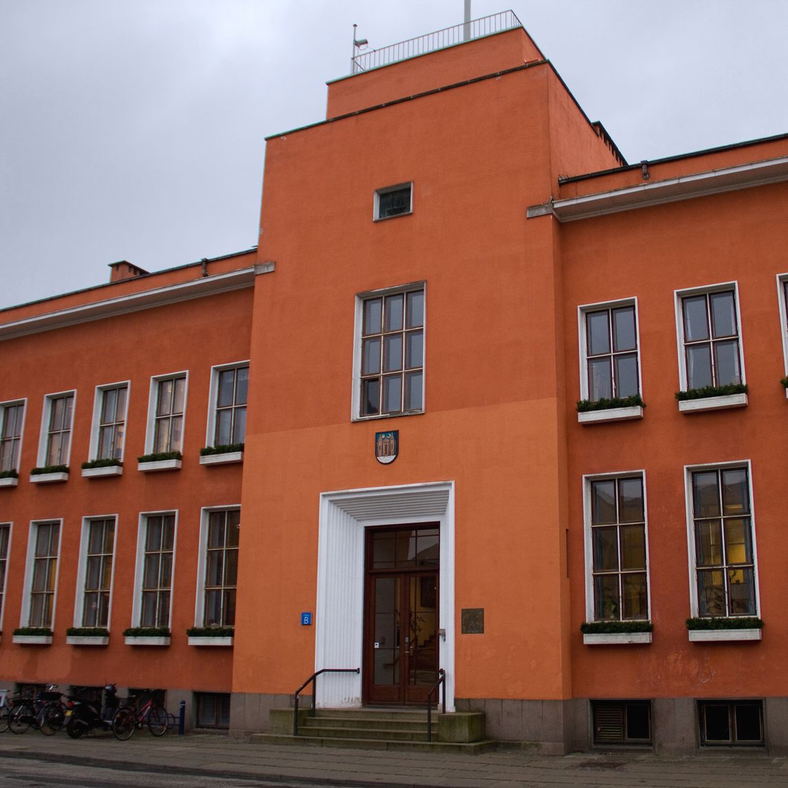 En stor rødlig bygning med brune og hvide vinduesrammer, der viser at bygningen har to etager.