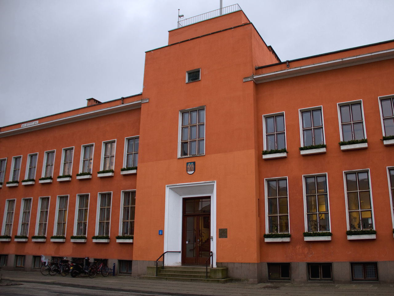 En stor rødlig bygning med brune og hvide vinduesrammer, der viser at bygningen har to etager.