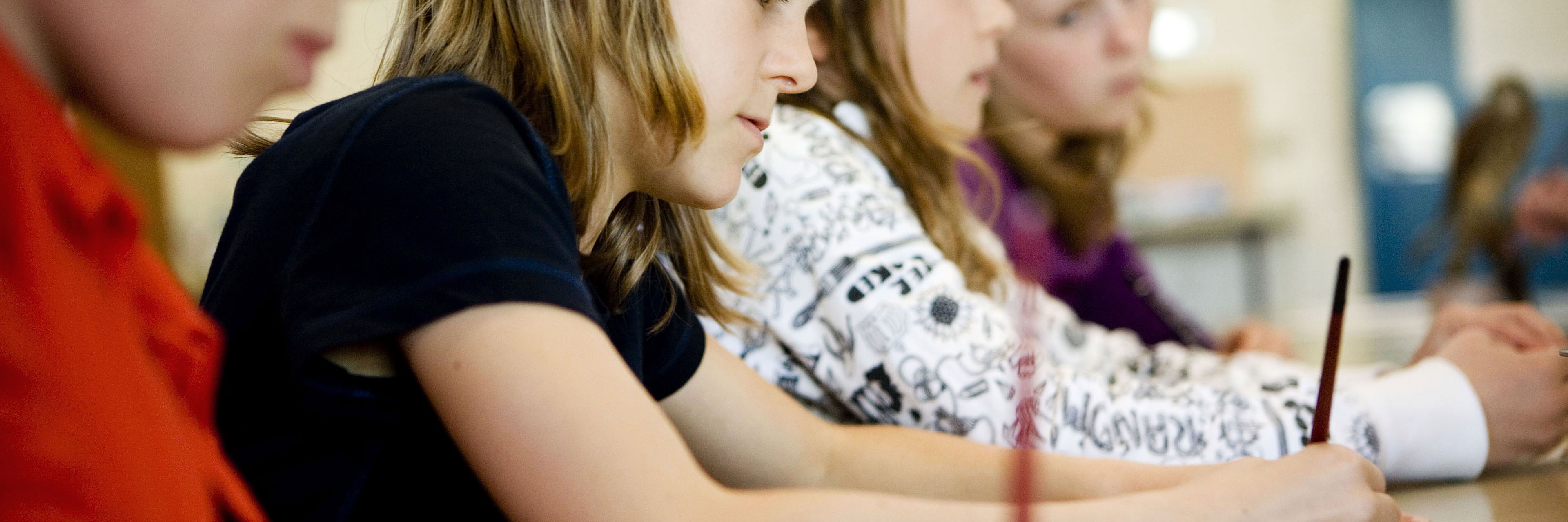 Fire skolelever sidder og skriver med hver deres blyant på et stykke papir.