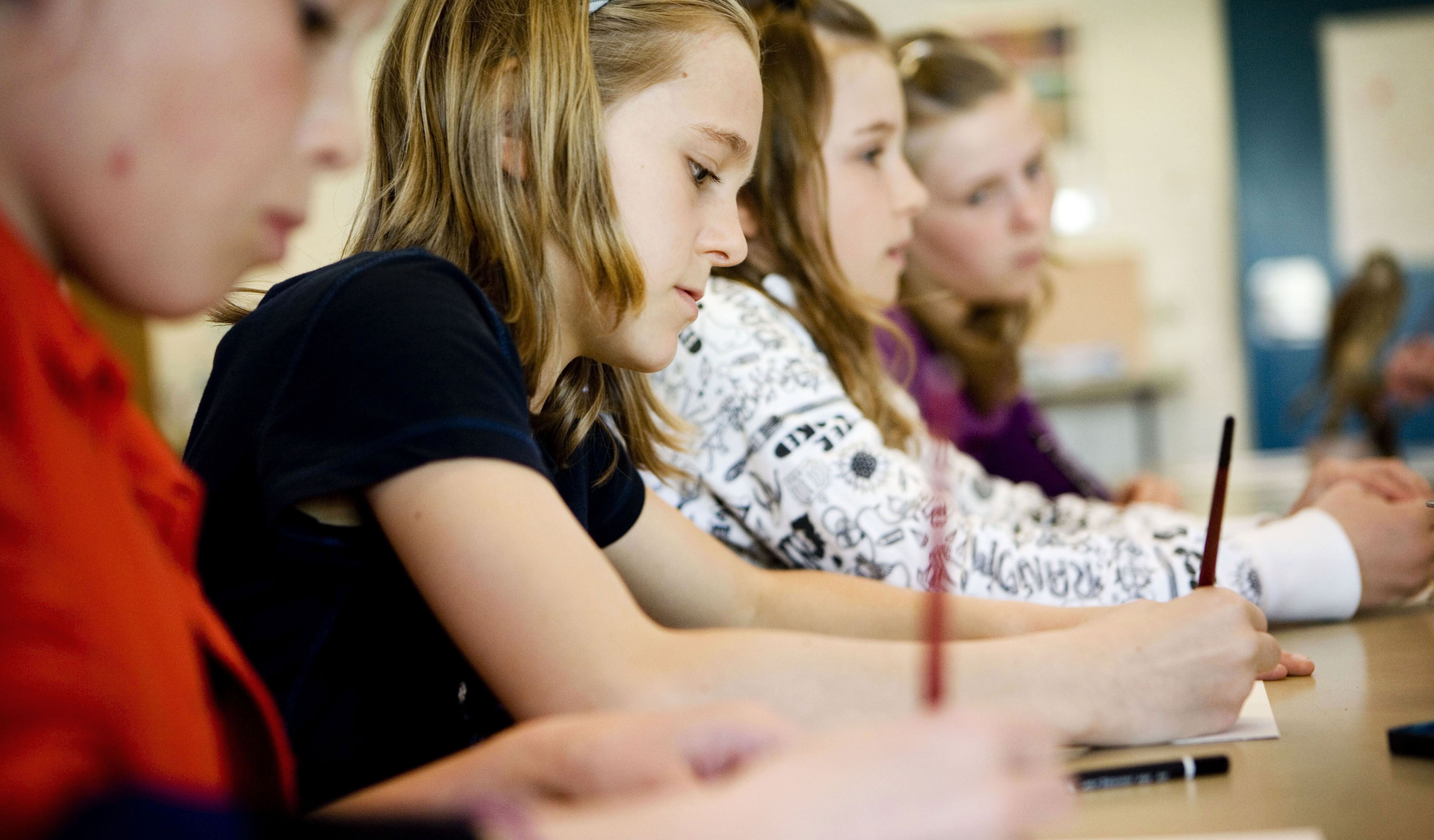 Fire skolelever sidder og skriver med hver deres blyant på et stykke papir.