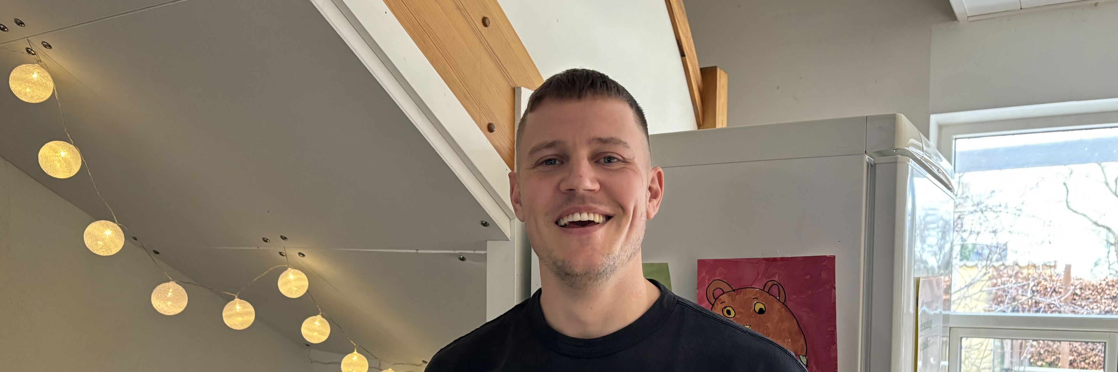 Ung smilende mand stående foran køleskab og bøger