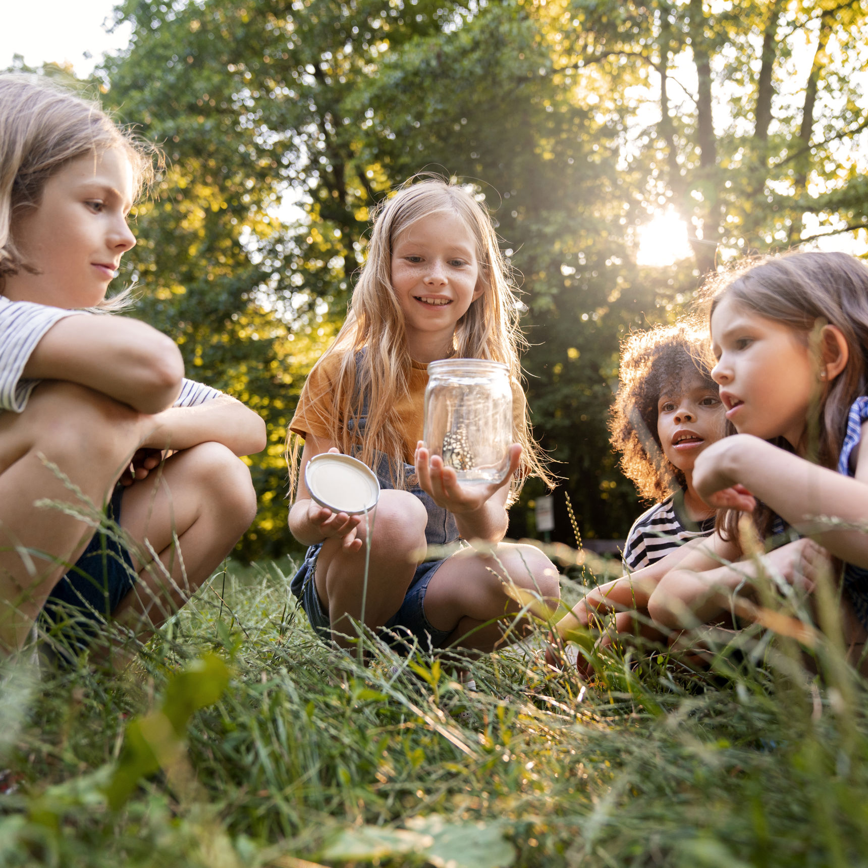 4 børn i rundkreds med sommerfugl i glas