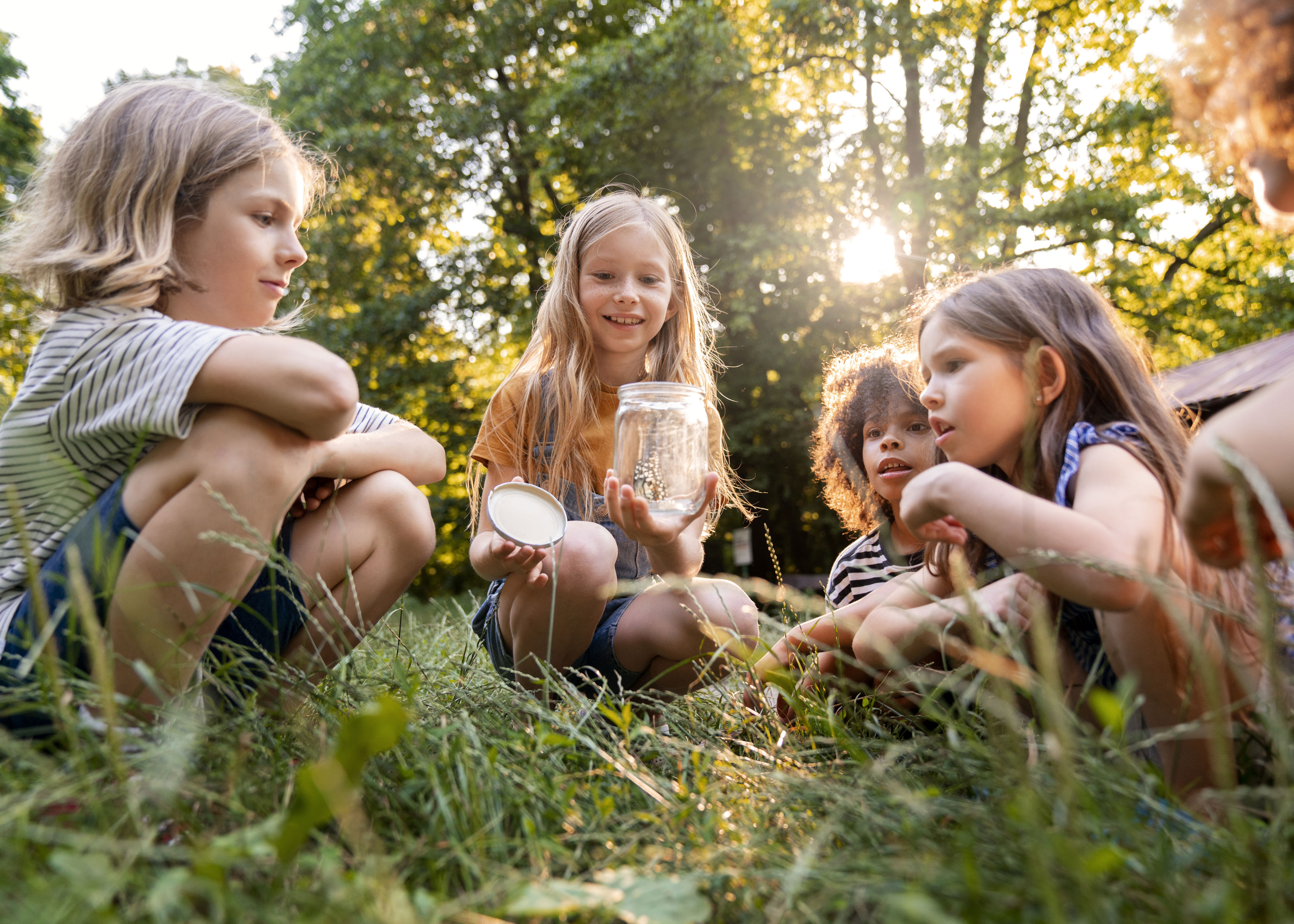 4 børn i rundkreds med sommerfugl i glas