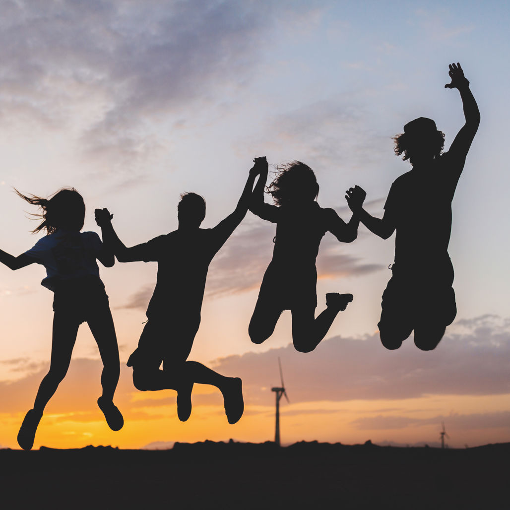 Dekorativt element - 4 hoppende unge mennesker i silhuet mod solnedgangshorisont