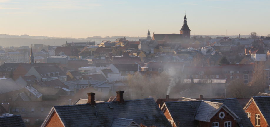 Foto over Svendborgs tage i morgendis med rygende skorstene og blå himmel