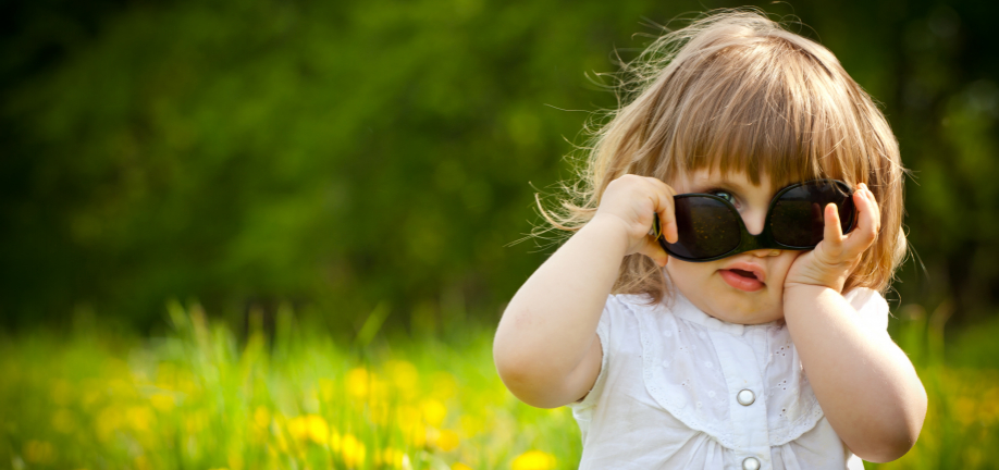 Barn i mælkebøttemark vender solbriller forkert